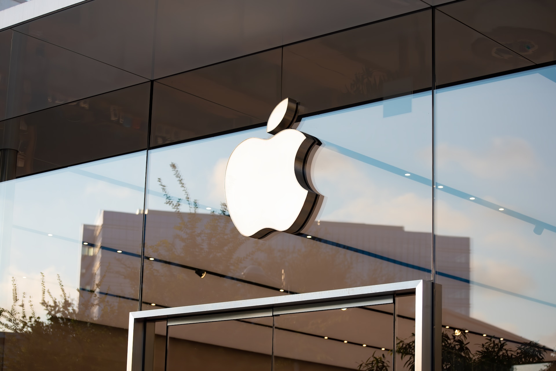 Photograph of the Apple store feature a white Apple logo against a glass window reflecting a cityscape