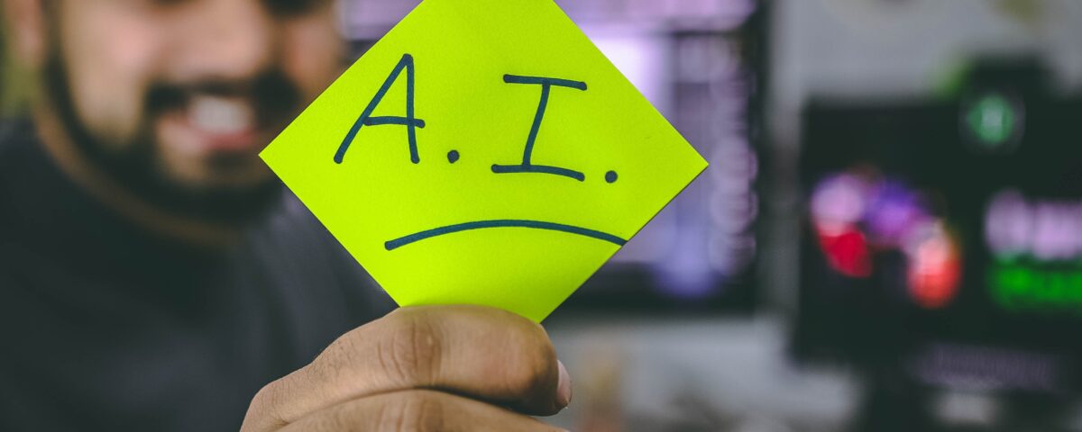 Photograph of a computer programmer holding up a sticky note that says "A.I."
