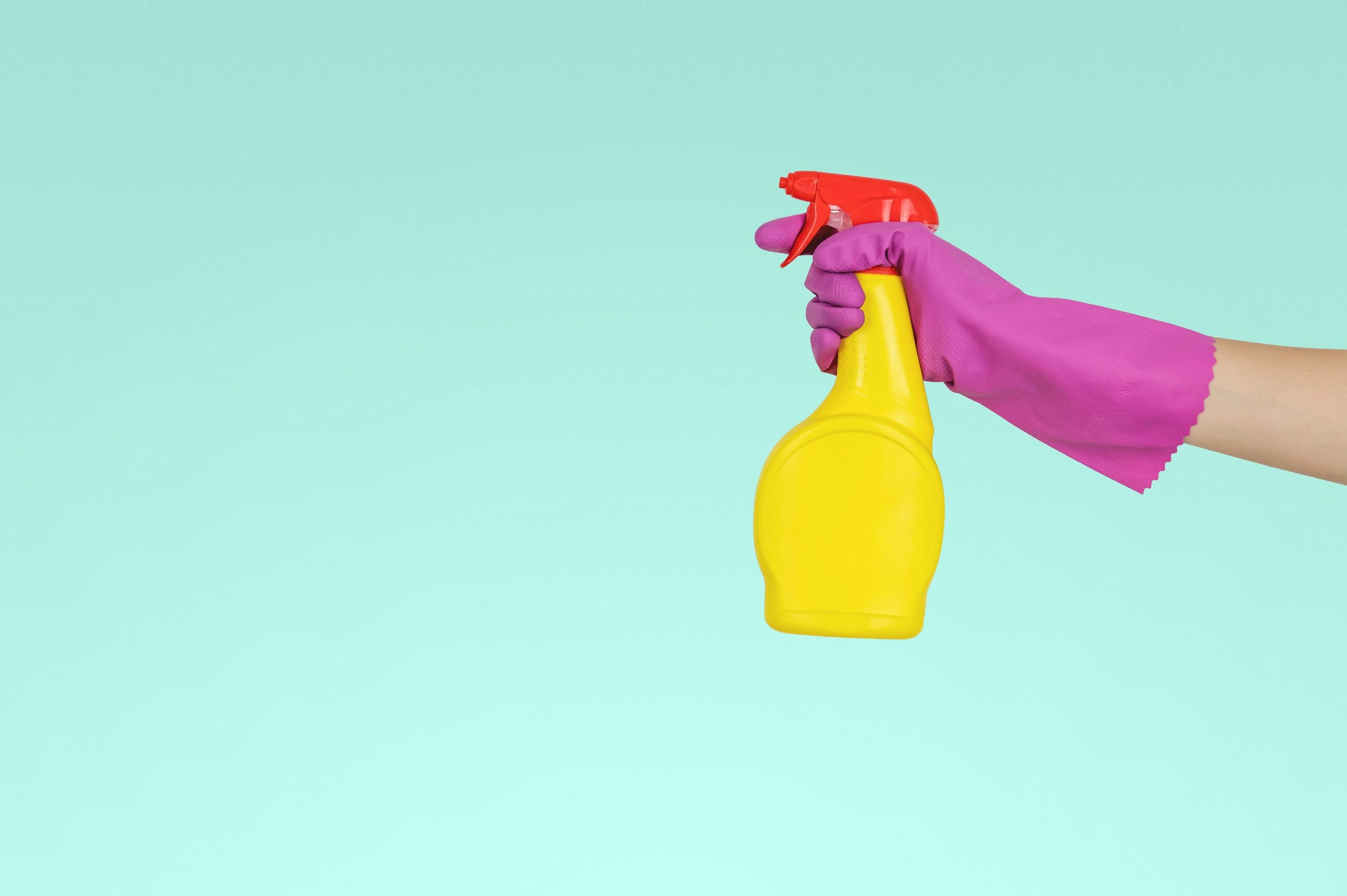 Hand in rubber glove holding a spray bottle of bleach