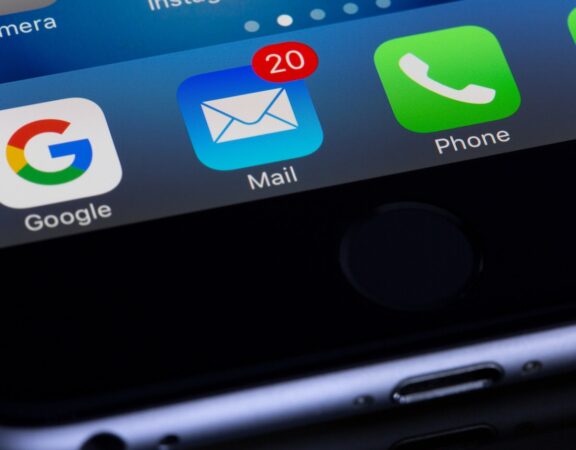 Photograph showing the bottom portion of an iPhone, particularly the email icon with a red notification.