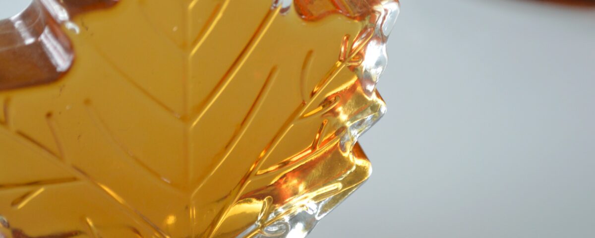 Photo of a glass, maple-leaf-shaped bottle containing maple syrup.