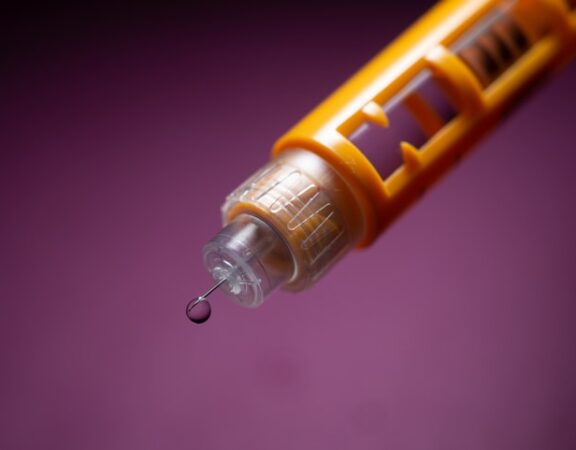 Photograph of an auto-injector needle with a drop of liquid at the tip of the needle.