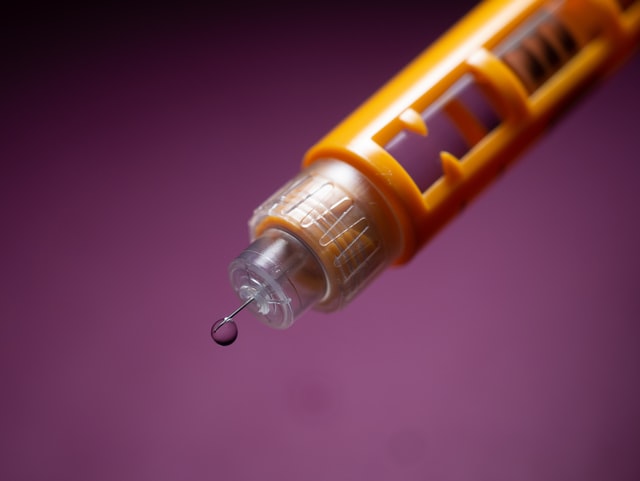 Photograph of an auto-injector needle with a drop of liquid at the tip of the needle.