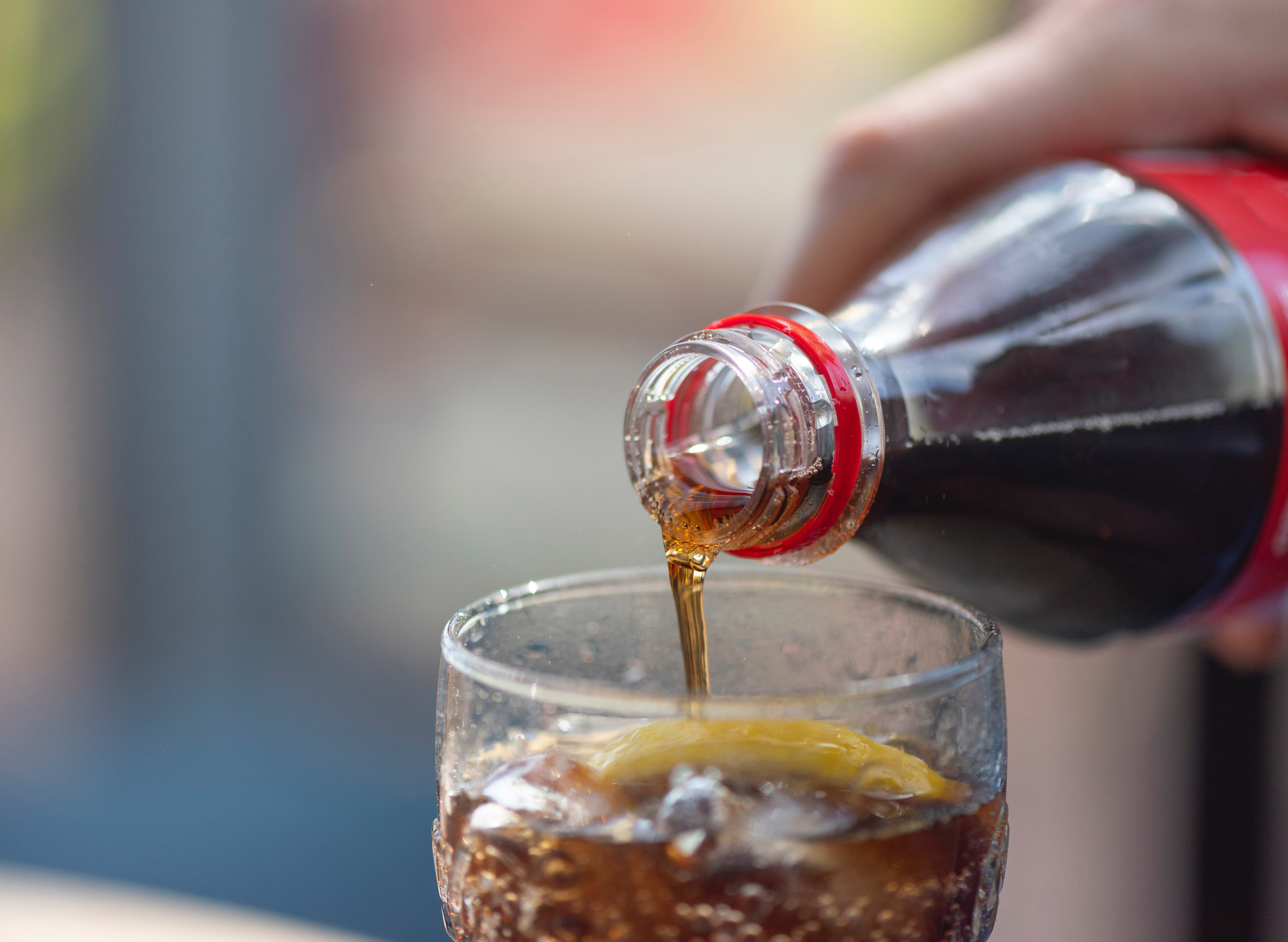 A Coke being poured from a plastic bottle into a glass with ice.