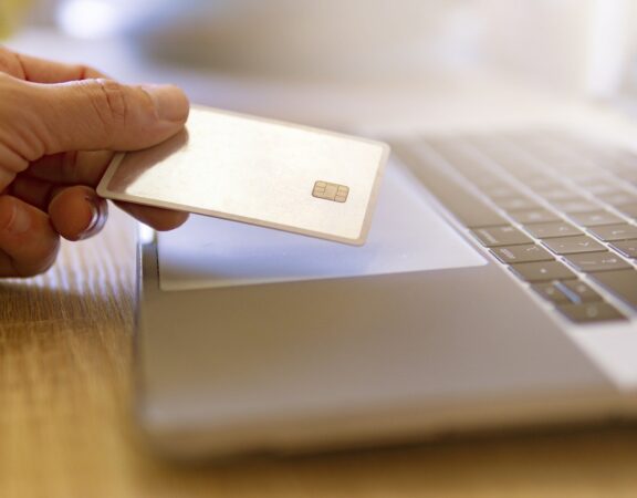 Photo of a hand holding a credit card above a laptop keyboard.
