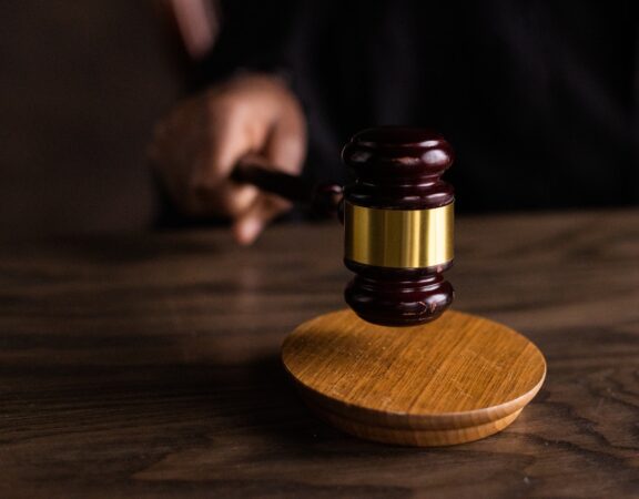 Photograph of a judge knocking a gavel on a wooden block against a dark background