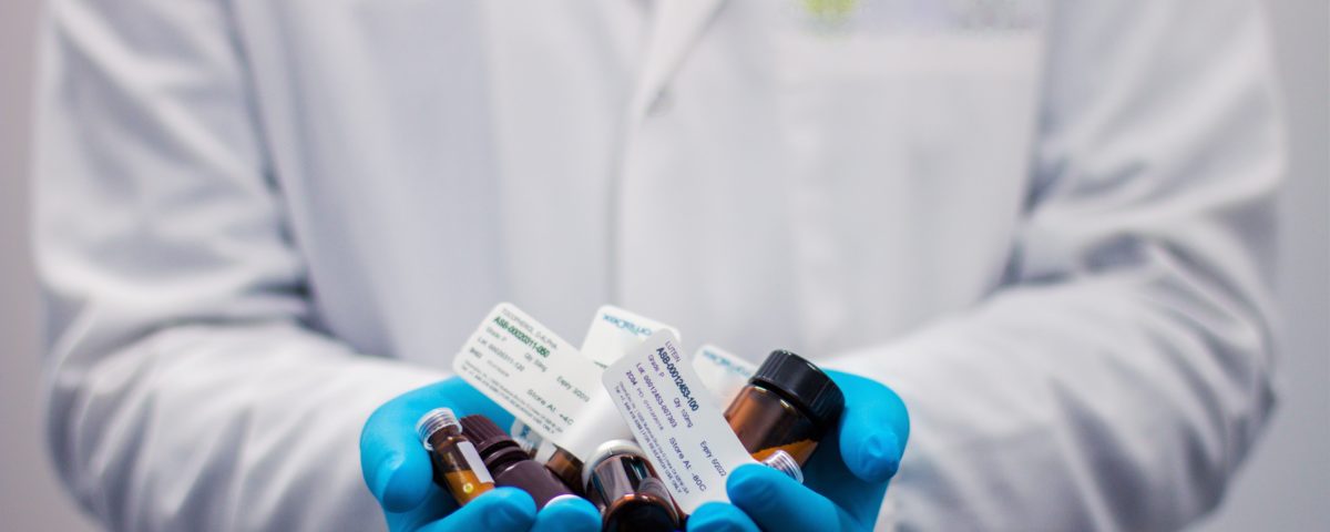 Pharmacist in a white lab coat, holding bottles of pharmaceuticals.