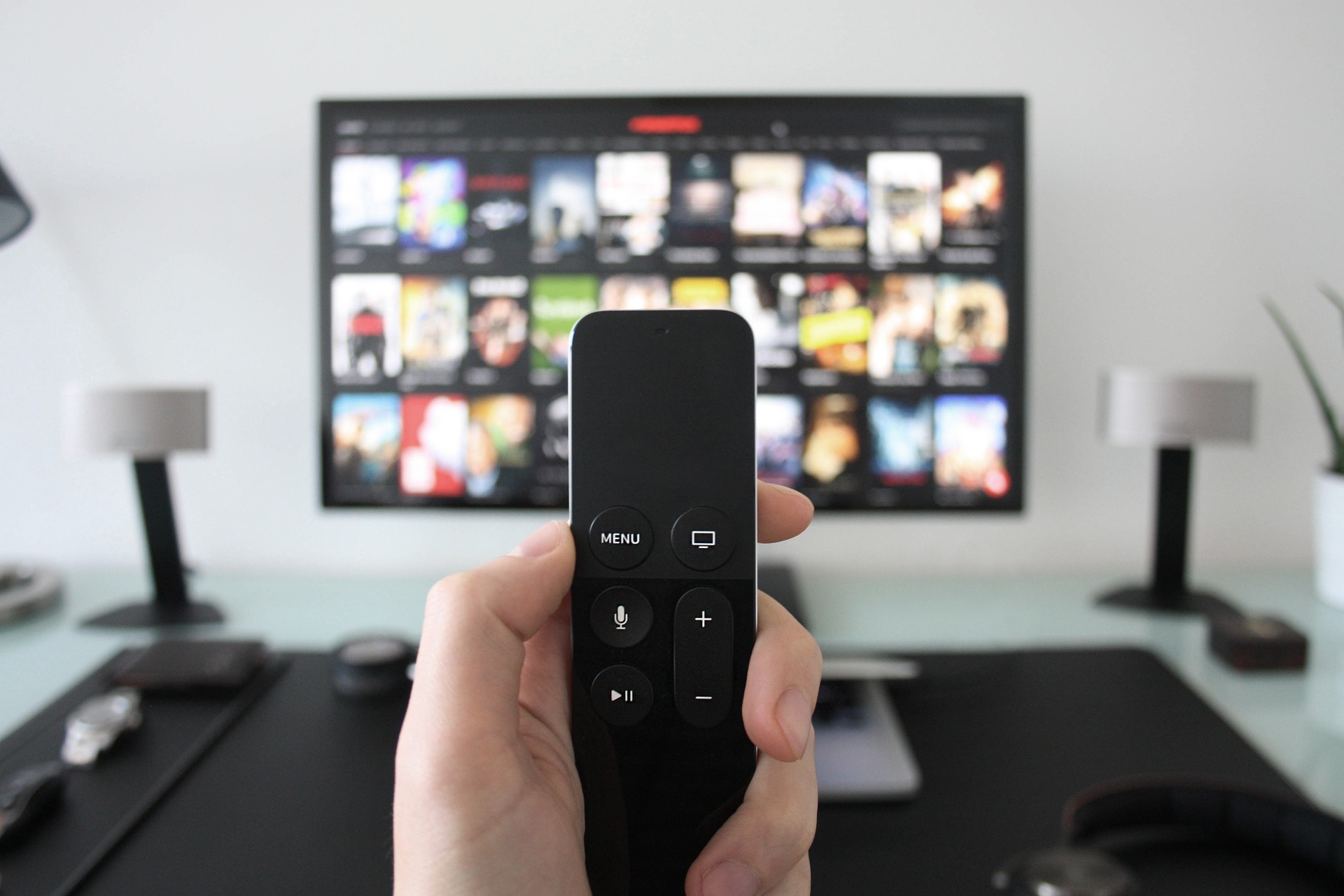 Photograph of a remote control for a smart tv pictured in front of a television screen displaying a streaming service.