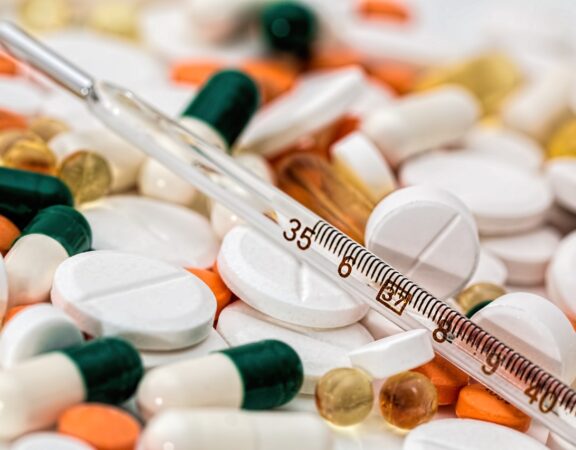 A thermometer is shown on a pile of pharmaceutical pills.