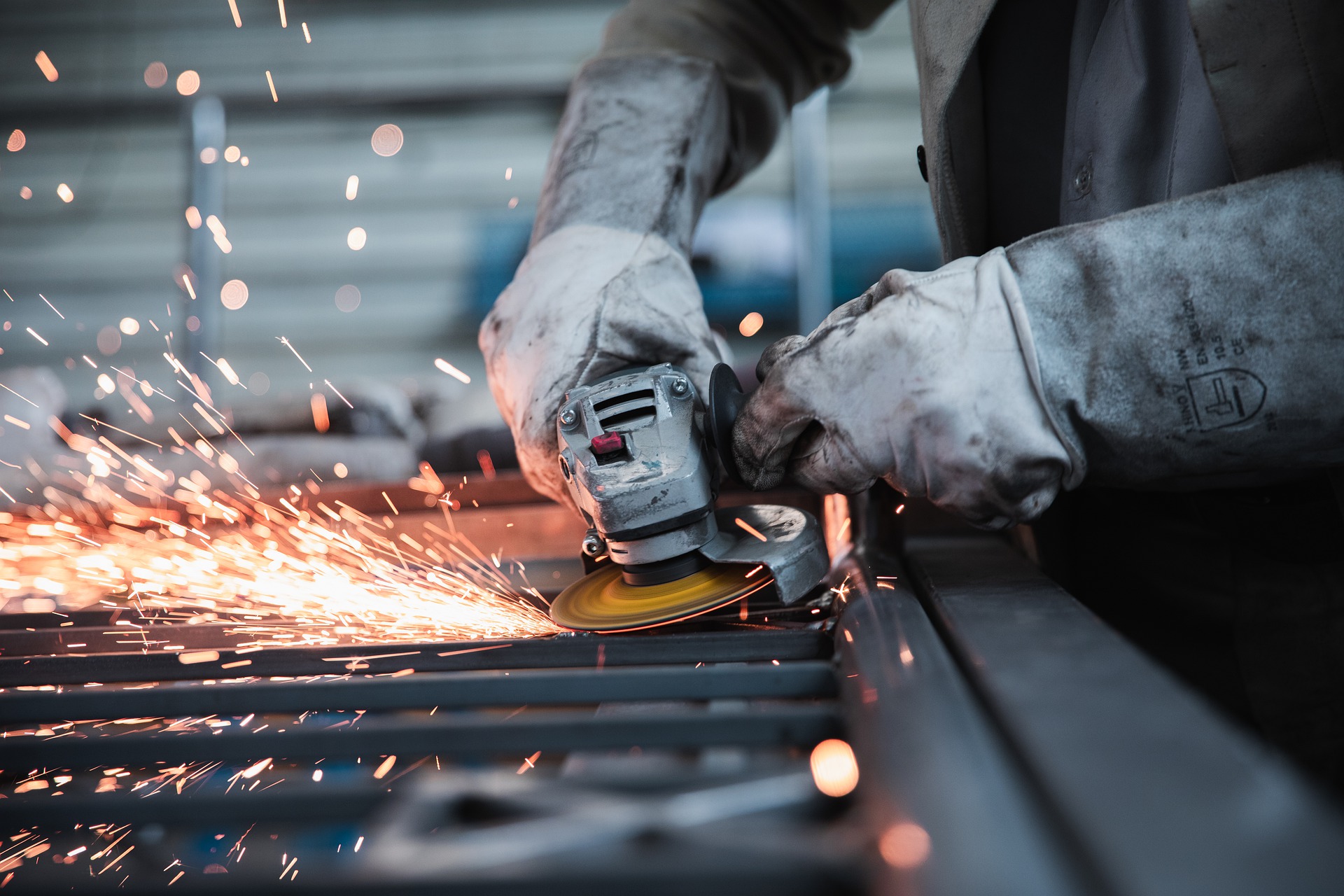 A metal worker using an angle grinder to cut steel.